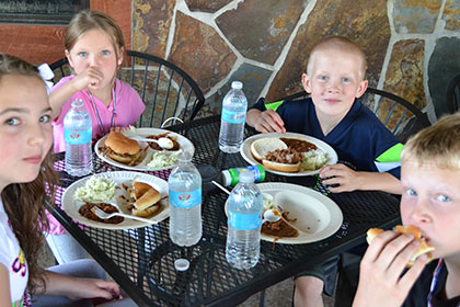 Children eating barbecue at a table outside.