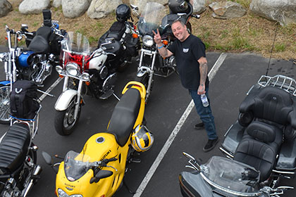 Man in parking lot standing next to motorcycles.