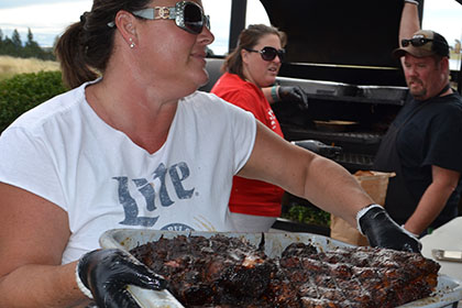 Woman holding a tub filled with barbecued meat.